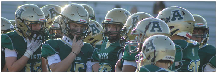 A group of people wearing green and gold football uniforms and helmets are gathered closely together on a field. Description generated by AI