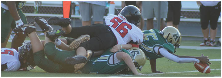 Several people wearing football uniforms and helmets are piled on the ground during a game on a grassy field. Description generated by AI