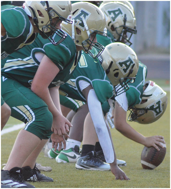 Three people in green football uniforms and helmets are crouched in a ready position on a football field. Description generated by AI