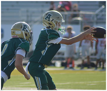 Two people wearing green football uniforms and gold helmets are engaged in a play on a football field. Description generated by AI