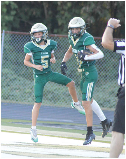 A person in a green football uniform with the number five is jumping on a field near a chain-link fence. Description generated by AI