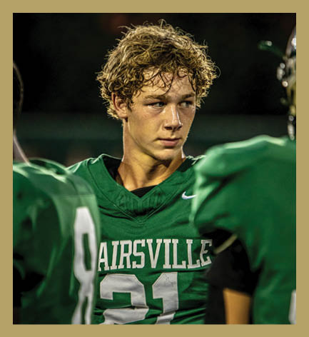 A person wearing a green football jersey with the number 21 and the word “AIRSVILLE" is standing among teammates also in green jerseys. Description generated by AI