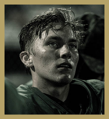 A person wearing a sports jersey looks upward with a focused expression, appearing sweaty and intense in a dimly lit setting. Description generated by AI
