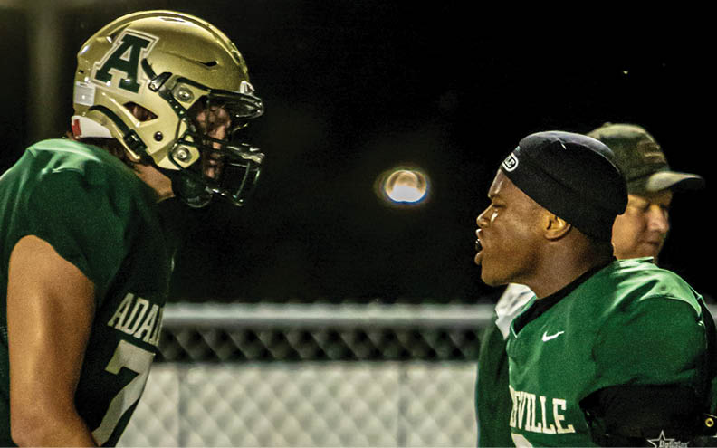 Three people wearing green football uniforms stand on a field with a chain-link fence in the background. Description generated by AI
