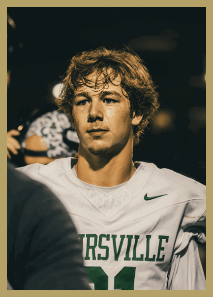 A person with tousled hair wearing a white sports jersey is looking intently at another person in a dimly lit setting. Description generated by AI