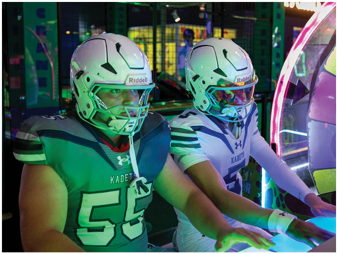 Three football players in blue and white uniforms running on a field. Description generated by AI