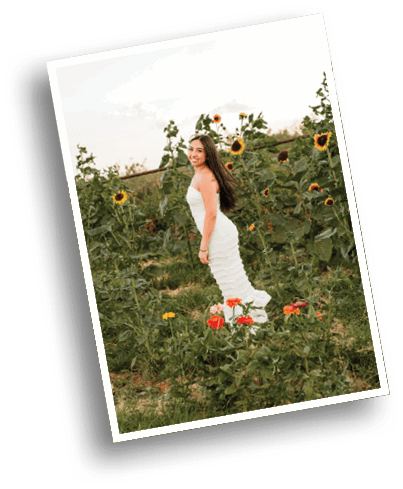 A person with long hair wearing a white dress is standing and smiling in a field of sunflowers and other wildflowers. Description generated by AI