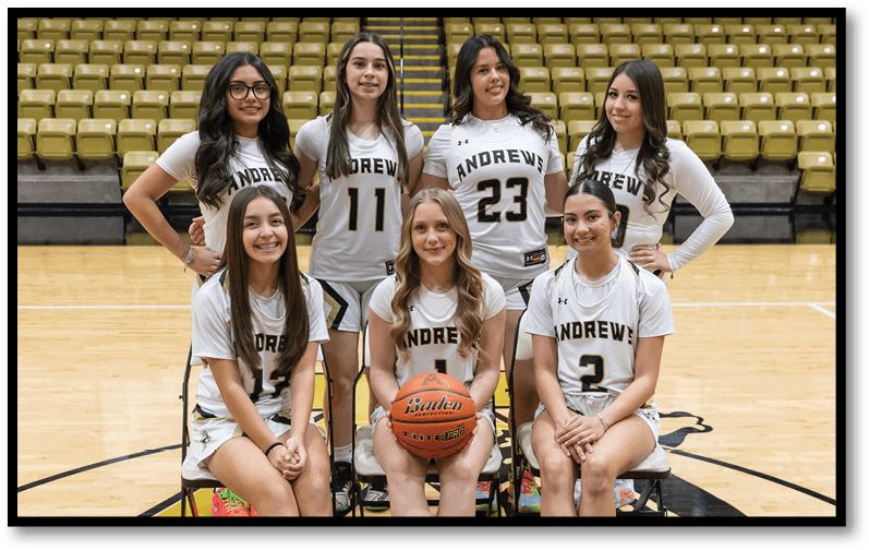 Seven people wearing matching sports uniforms with the word Andrews pose together on a basketball court with one person holding a basketball. Description generated by AI