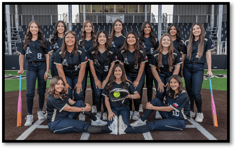 A group of people in matching dark sports uniforms pose on a softball field with bats and a softball glove, smiling in a team formation. Description generated by AI