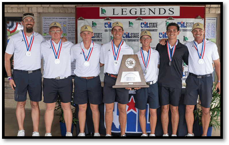 Seven adults wearing matching white shirts, dark shorts, and medals stand together smiling, with one holding a large trophy in front of a backdrop labeled “LEGENDS" and a tournament logo. Description generated by AI