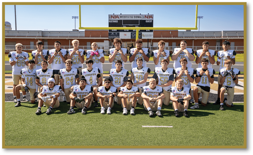 A group of people wearing football uniforms pose together on a football field with a scoreboard and goalposts in the background. Description generated by AI