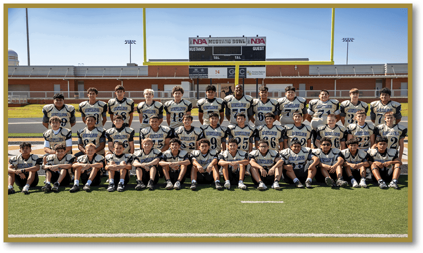 A group of people wearing matching sports uniforms is posed in rows on a football field with a scoreboard and goalposts in the background. Description generated by AI