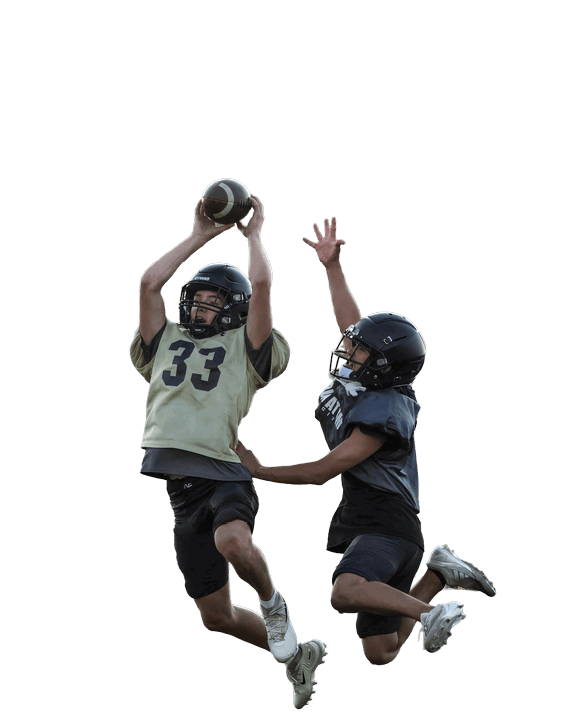 Two people wearing helmets and sports gear are jumping in the air on a football field, with one catching a football while the other reaches up to block or intercept. Description generated by AI