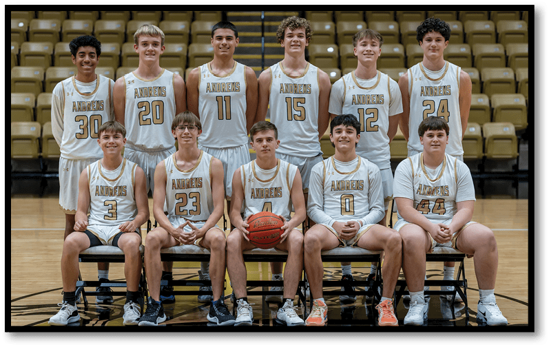 A group of basketball players in white uniforms with “Andrews" on the front pose together in a gym with some seated on chairs holding a basketball and others standing behind them. Description generated by AI