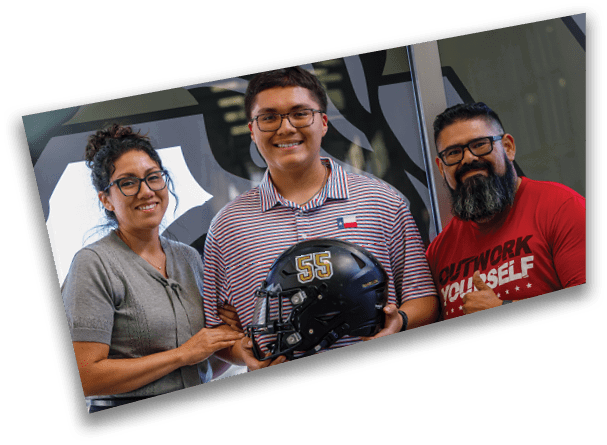 Three people stand together indoors with one person holding a black football helmet marked with the number 55 while another person wearing glasses and a beard gives a thumbs-up. Description generated by AI