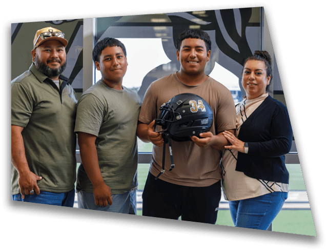 Three adults stand indoors near a window with one holding a black football helmet with the number 34 on it while the others smile and pose closely. Description generated by AI