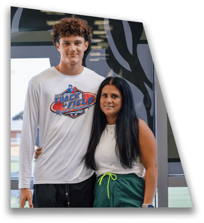 Two people stand close together smiling, with one wearing a white shirt featuring a colorful track and field championship logo. Description generated by AI
