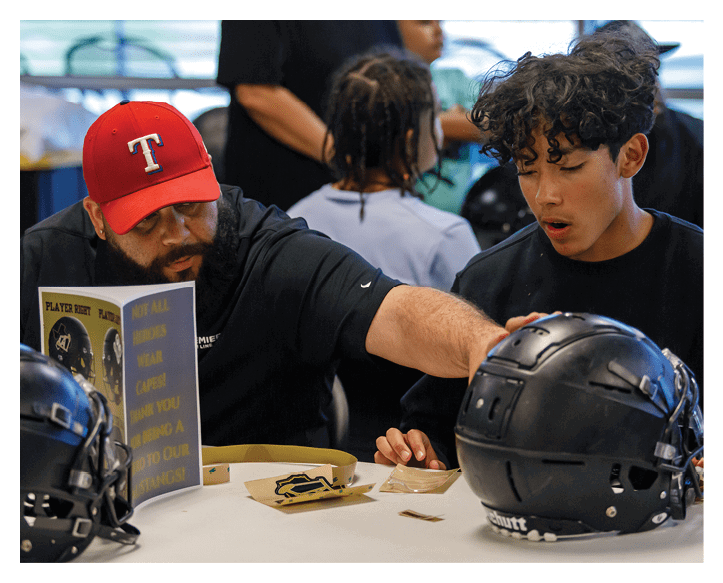 Four people stand closely together indoors with one person holding a black sports helmet with the number 25 on it. Description generated by AI