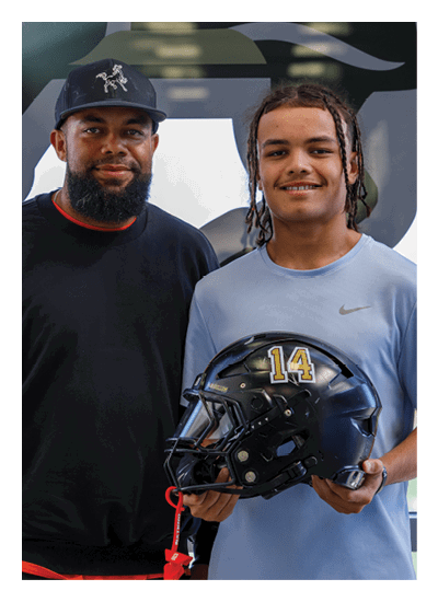 Two people are closely examining a black football helmet indoors, with one person holding it up and the other looking at it attentively. Description generated by AI