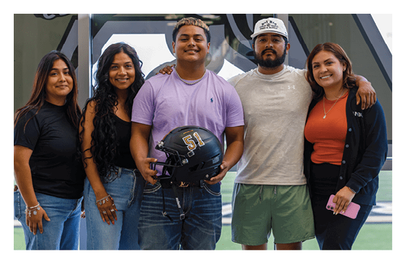 Five people stand closely together smiling indoors with one person holding a black sports helmet. Description generated by AI