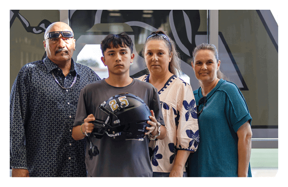 Four people stand indoors with one person holding a black football helmet with the number 25 on it, all looking toward the camera. Description generated by AI