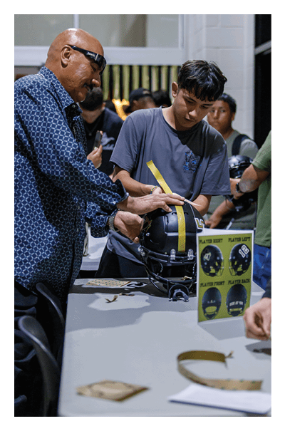 Two adults are adjusting or holding a black sports helmet with a yellow stripe. Description generated by AI