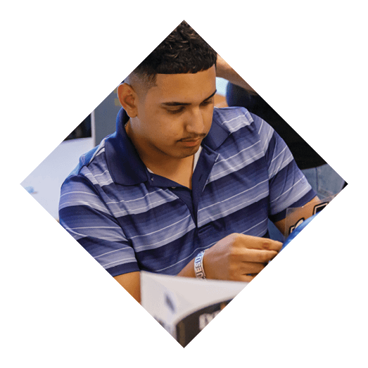 A person with short curly hair wearing a blue striped polo shirt is focused on reading or examining something in their hands while sitting indoors. Description generated by AI