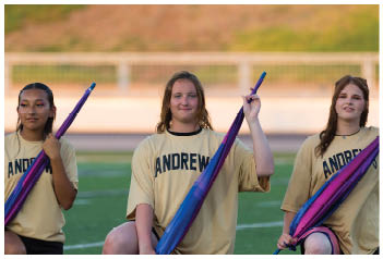Two people wearing matching yellow shirts with the word “ANDREW" hold colorful flags while standing outdoors on a field. Description generated by AI