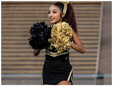 A person wearing a cheerleading uniform is holding gold pom-poms. Description generated by AI