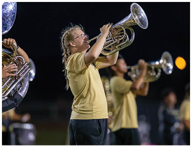 People wearing yellow shirts are playing brass instruments outdoors at night. Description generated by AI