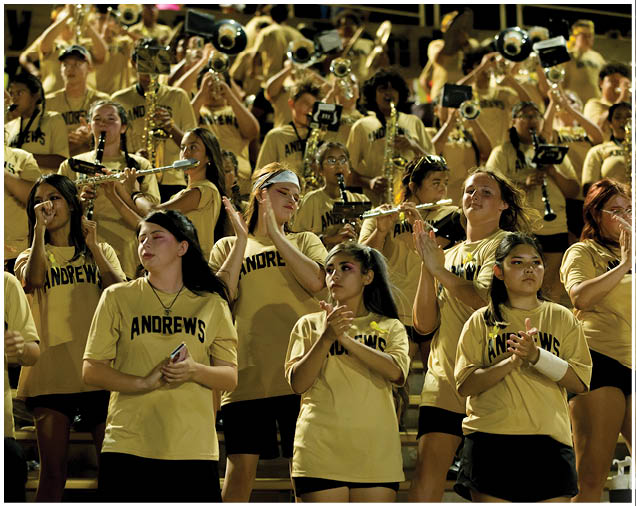 A person wearing a yellow shirt is playing a sousaphone in a marching band with other musicians in the background. Description generated by AI