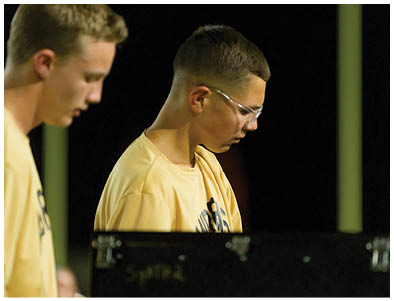 Two adults wearing yellow shirts are focused on an activity involving a black object in front of them against a dark background. Description generated by AI