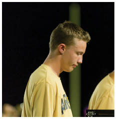 Two people wearing yellow shirts with text on them are standing side by side, looking down at something in front of them. Description generated by AI