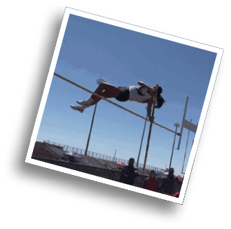 Two people stand near a pole vault setup on an outdoor track and field area with bleachers and a clear sky in the background. Description generated by AI