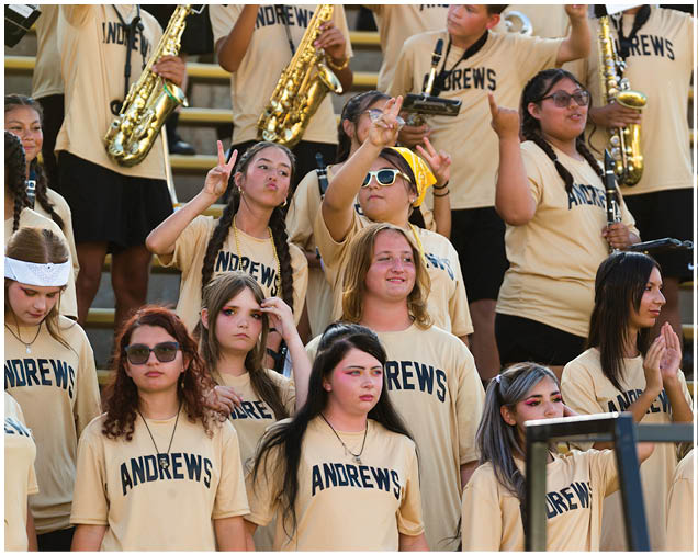 A group of people wearing matching Andrews t-shirts are gathered in bleachers, some holding musical instruments and others making hand gestures or clapping. Description generated by AI