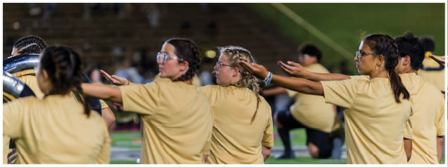 A group of people wearing matching yellow shirts are standing in a line outdoors with their arms extended forward, appearing to participate in a coordinated activity. Description generated by AI