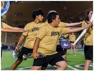 People wearing matching yellow shirts with “ANDREW" printed on them are performing a coordinated movement on a sports field at night. Description generated by AI