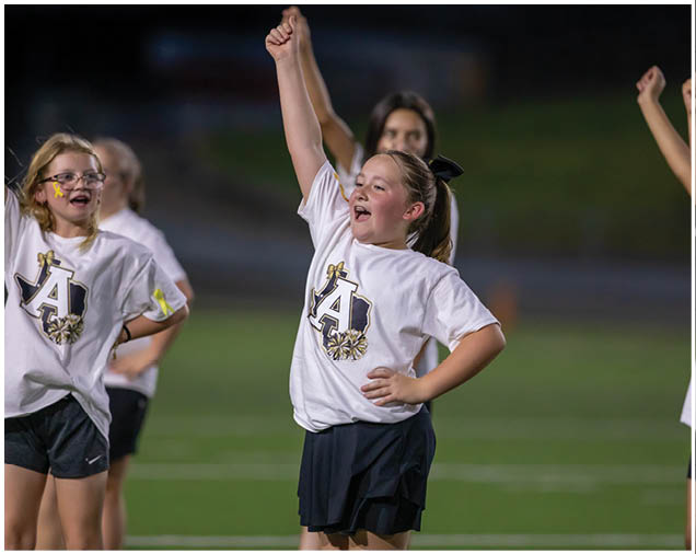 Children wearing matching cheerleading outfits are enthusiastically raising their arms while performing on a field. Description generated by AI