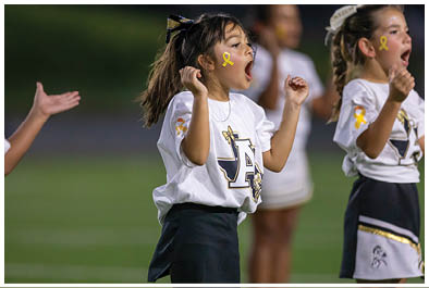 Children in cheerleading uniforms with yellow ribbons on their faces are enthusiastically cheering on a field. Description generated by AI