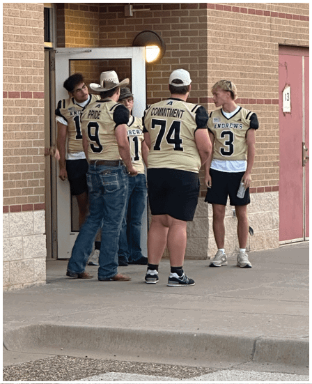 A group of people wearing sports jerseys and casual clothing stand outside a building with brick walls and a concrete sidewalk. Description generated by AI