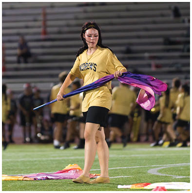 A person wearing a yellow shirt with the word “ANDREWS" printed on it is looking down while holding a purple fabric. Description generated by AI