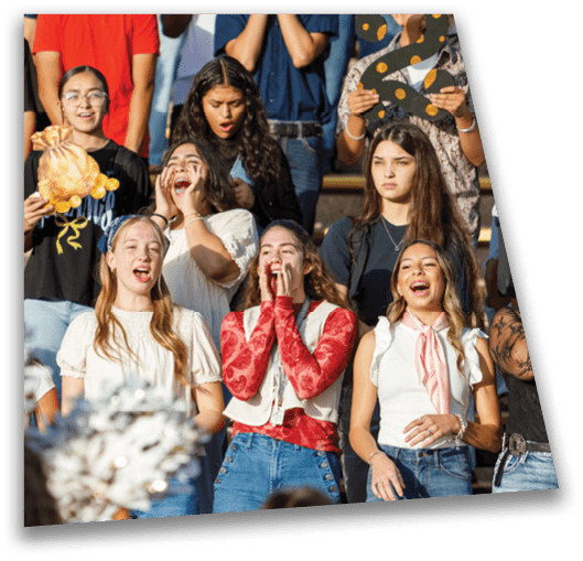 A group of people enthusiastically cheering and holding pom-poms and a stuffed animal in an outdoor setting. Description generated by AI