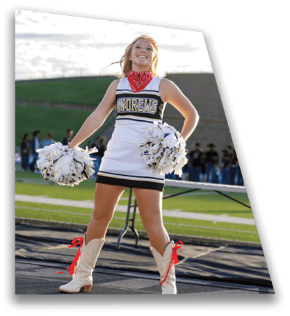 A person wearing a cheerleading uniform with the word “ANDREWS" and a red bandana is standing outdoors on a track field holding white pom-poms. Description generated by AI