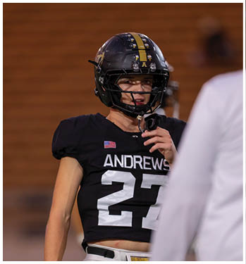 A close-up of a black football helmet with a yellow stripe down the center and small Texas state flag decals on the top. Description generated by AI