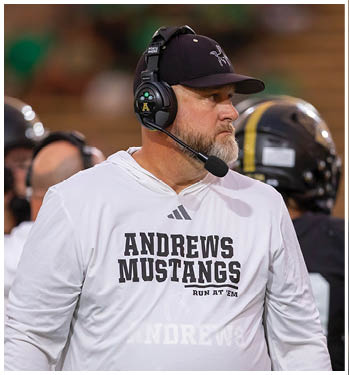 A person wearing a black cap with a horse logo and a headset labeled “PORTA PHONE" and "HEAD COACH" is looking intently to the side. Description generated by AI