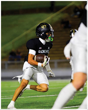A person wearing a black football helmet with a green mouthguard is on a field with blurred background elements. Description generated by AI