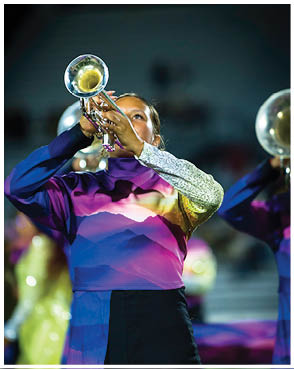 A person in a colorful uniform with a mountain landscape design is playing a trumpet during a nighttime performance. Description generated by AI