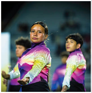 People wearing colorful gradient uniforms with sequined sleeves perform a synchronized routine outdoors. Description generated by AI