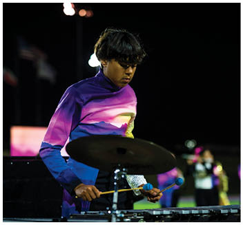 A person wearing a colorful uniform is playing a percussion instrument with mallets during a nighttime outdoor event. Description generated by AI