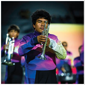 A person wearing a colorful uniform is playing a trumpet in a marching band with other band members visible in the background. Description generated by AI